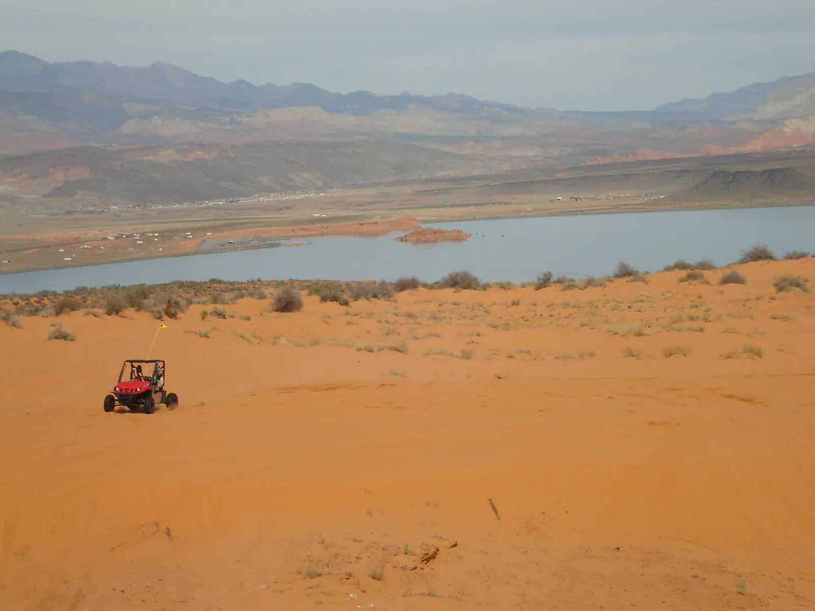Orange sand sloping down to Sand Hollow Reservoir with mountains beyond